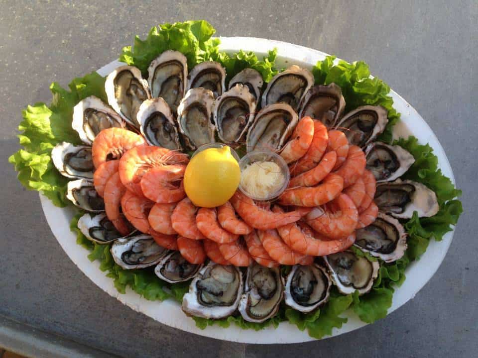Plateau ovale de fruits de mer: huîtres fraîches sur lit de laitue entourant une pile de crevettes roses cuites, avec citron et sauce.